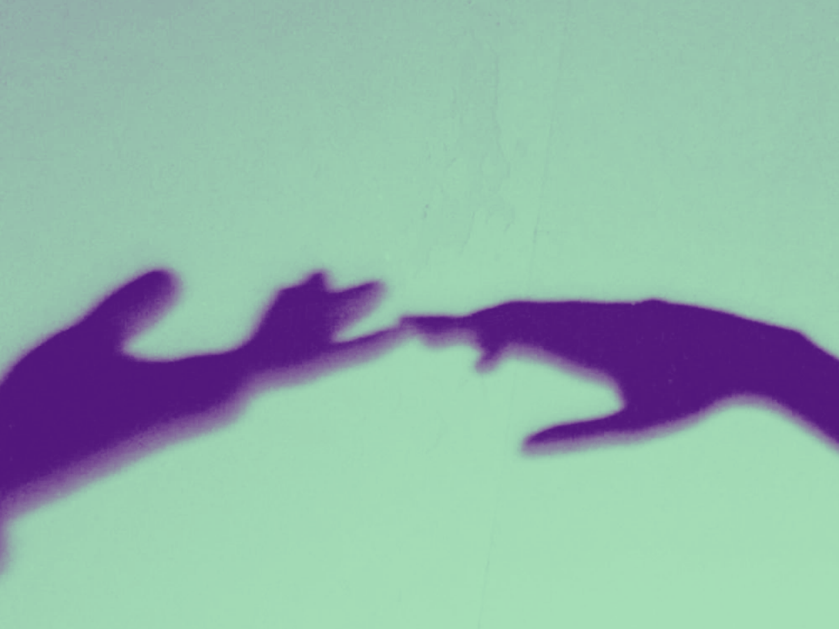 Grainy mint green and purple duotone photo of two hand shadows reaching toward each other across a pale wall, fingertips nearly touching.