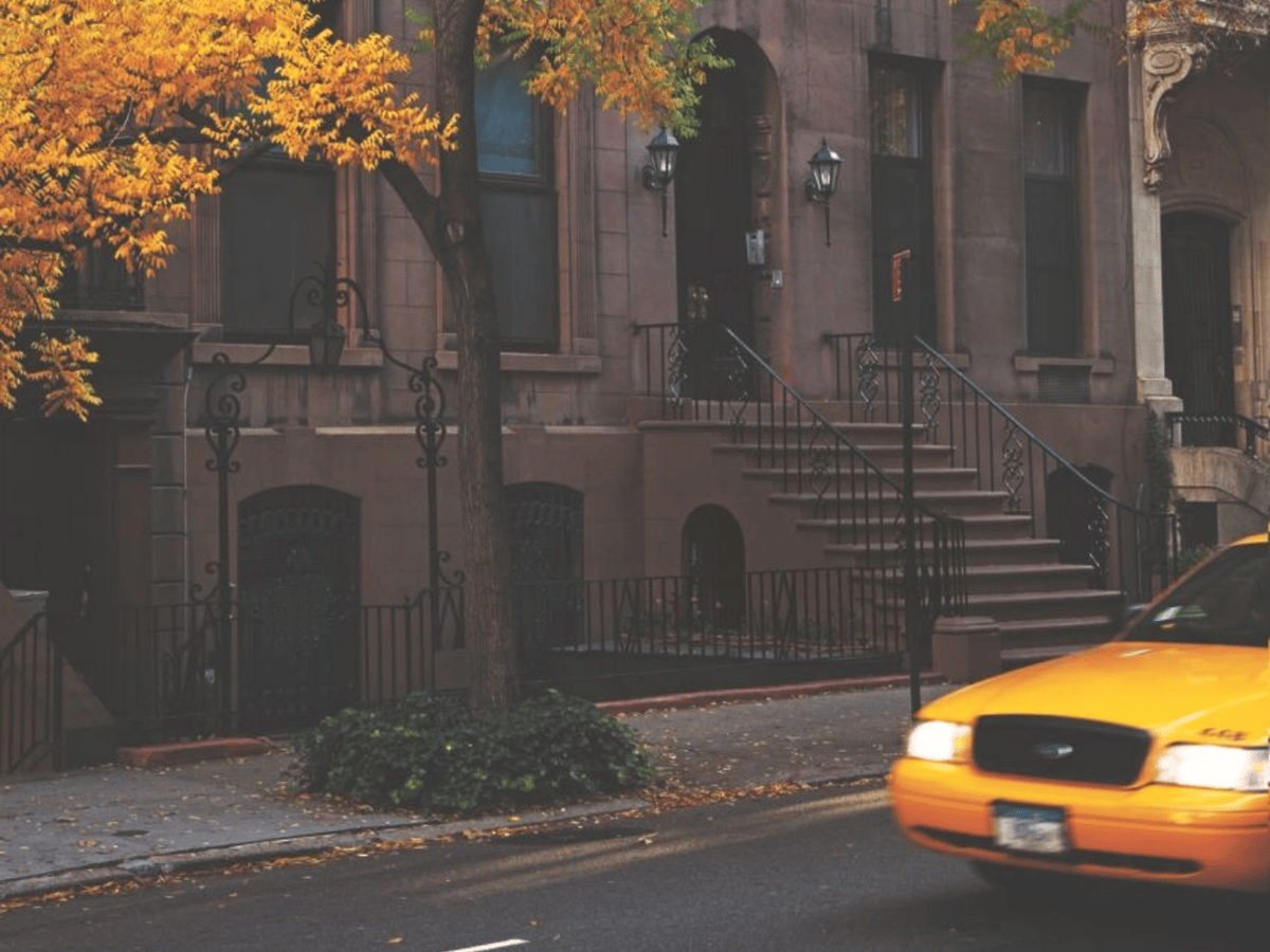 A Chelsea brownstone block in early fall with a taxi passing